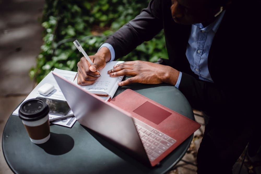 pessoa com um notebook anotando em um caderno o passo a passo para organizar um evento corporativo